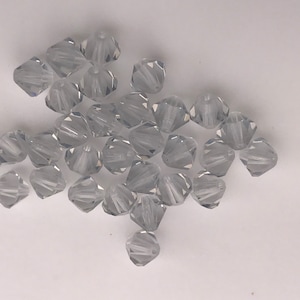 May include: A pile of clear glass beads with a faceted, teardrop shape. The beads are scattered on a white surface.