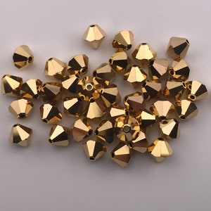 May include: A group of gold-colored glass beads with a faceted, pointed design. The beads are scattered on a white surface.