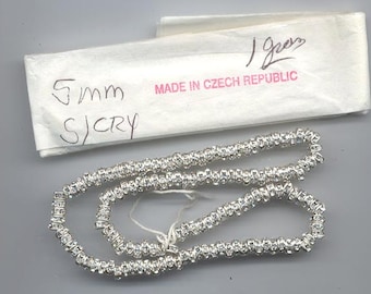 Puede incluir: Una hebra de cuentas de cristal cuadradas de color plateado. Las cuentas miden aproximadamente 5 mm y están enhebradas en un hilo transparente. El embalaje dice "5mm  SICRY MADE IN CZECH REPUBLIC".