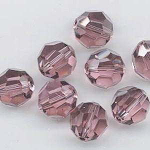 May include: A group of eight faceted glass beads in a light purple color. The beads are round and have a smooth, shiny finish.