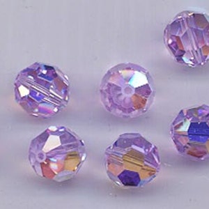 May include: A collection of faceted, iridescent beads in shades of lavender and purple. The beads have multiple facets that catch the light, creating a shimmering effect. These beads are suitable for jewelry making and crafts.
