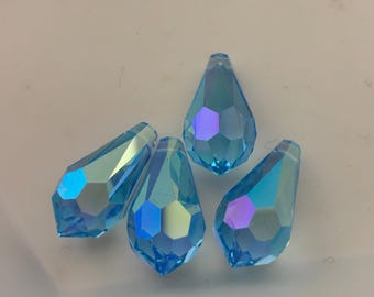 May include: Four faceted, teardrop-shaped beads in shades of light blue with iridescent highlights. The beads have a hexagonal pattern and are arranged on a white surface. These beads are suitable for jewelry making.