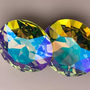 Puede incluir: Dos piedras de vidrio ovaladas iridiscentes con un arcoíris de colores, incluyendo verde, azul, amarillo y morado.