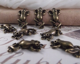 May include: A collection of eight antique bronze frog charms. The frogs are in various poses, some with their legs outstretched and others with their legs tucked in. The charms are a great addition to any jewelry making project.