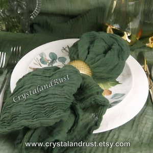 May include: A dark green fabric napkin tied around a gold napkin ring on a white plate with a floral design. The plate is on a green tablecloth. The text "CrystalandRust" and "www.crystalandrust.etsy.com" is visible on the image.