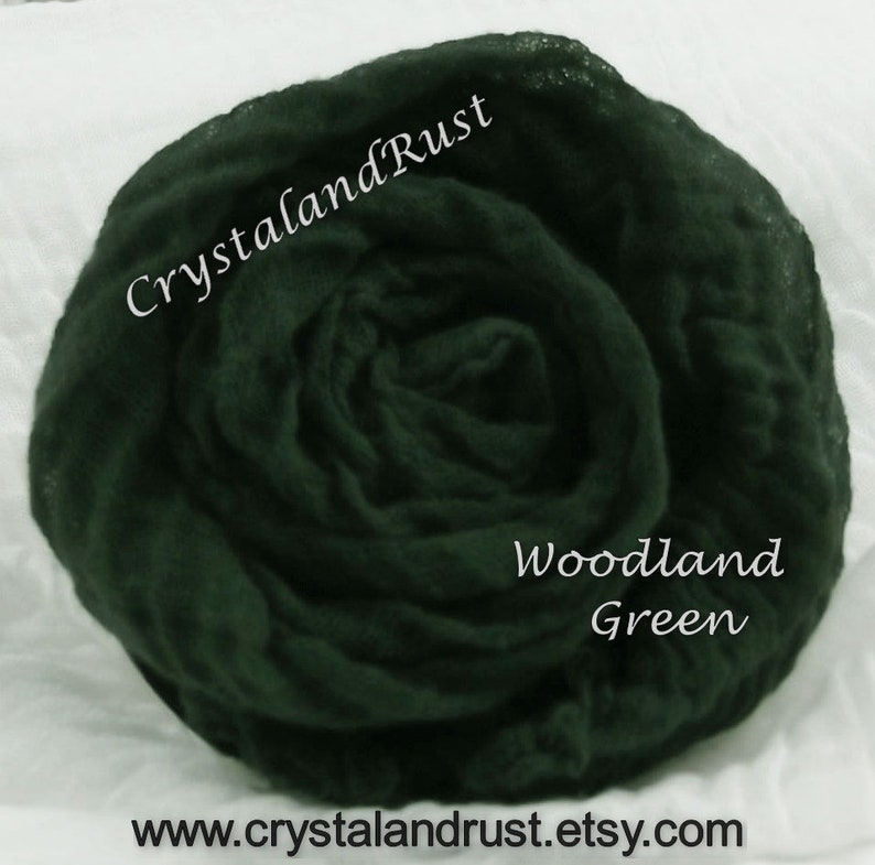 May include: A dark green, crinkled fabric backdrop, also known as a photography backdrop, for use in photography. The fabric is gathered in a rose-like shape. The text "Woodland Green" is written on the fabric. The text "CrystalandRust" is written on the fabric.