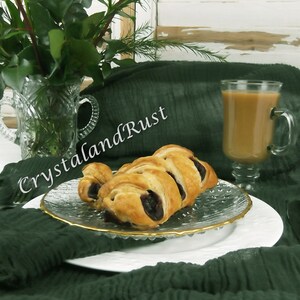 May include: Two pastries filled with blueberries on a white plate with a gold rim. The plate is on a green tablecloth with a glass of coffee in the background. The text "CrystalandRust" is visible in the image. The website address "www.crystalandrust.etsy.com" is also visible in the image.