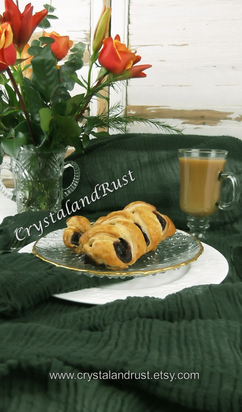 May include: Two pastries filled with blueberries on a white plate with a gold rim. The plate is on a green tablecloth with a glass of coffee in the background. The text "CrystalandRust" is visible in the image. The website address "www.crystalandrust.etsy.com" is also visible in the image.