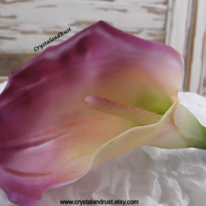 May include: A single artificial calla lily flower with a deep purple and white color gradient. The flower is lying on a white textured surface.