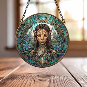 May include: Round stained glass art piece featuring a Na'vi woman from the movie Avatar. The artwork is framed in a bronze-colored metal and has a chain for hanging. The design incorporates blue, teal, and purple floral elements, with a detailed portrait at the center.