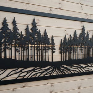 Könnte beinhalten: Schwarze Metall-Wandkunst mit einer Waldszene, die hohe Bäume und detaillierte Wurzeln zeigt. Der rechteckige Rahmen umschließt die Silhouette, wodurch ein naturnahes Dekorationselement entsteht.