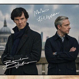 May include: A framed print featuring two men in coats, with signatures in white. One man wears a dark coat and scarf, the other a navy jacket. The background shows a cityscape with a domed building.