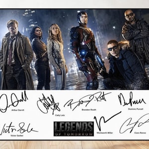 May include: A framed poster featuring the cast of "Legends of Tomorrow." The image shows a group of actors in costume, with signatures of the cast members below the image. The show's logo is also visible.