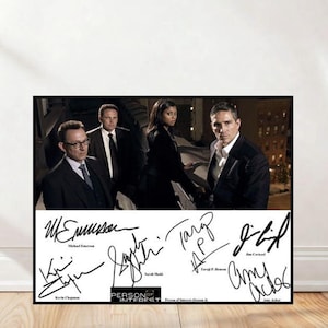 Puede incluir: Un póster enmarcado con un grupo de cuatro personas vestidas con trajes, con un telón de fondo de la ciudad. Debajo de la imagen hay firmas y el texto "PERSON OF INTEREST". Las firmas incluyen a Michael Emerson, Kevin Chapman, Sarah Shahi, Taraji P. Henson, Jim Caviezel y Amy Acker.