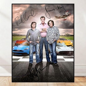 May include: A framed poster featuring three men standing in front of several sports cars. The poster has signatures in black ink and a small airplane graphic. The cars are in various colors, including blue, orange, and yellow.