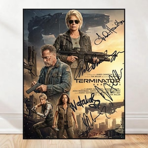 May include: A framed movie poster for "Terminator: Dark Fate" featuring actors with autographs. The poster shows the main characters holding weapons, with the film's title and credits at the bottom. The background depicts a futuristic cityscape.