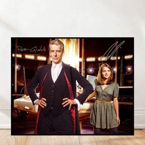 May include: A framed poster featuring two people, one in a black suit with a red lining and the other in a patterned dress. The poster has signatures in the top corners and is set against a detailed background.
