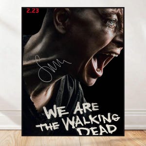 Peut inclure: A framed poster with a person's face in a distressed expression, mouth open. The poster reads "WE ARE THE WALKING DEAD" in white, stylized lettering. A signature is visible, along with the number "2.23" in the upper left corner.