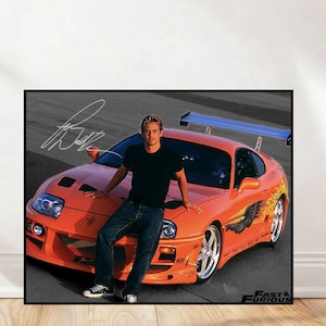 May include: A framed print featuring a vibrant orange sports car with a spoiler, and a person leaning against it. The car has custom graphics and chrome wheels. The print includes the text "Fast & Furious" and an autograph.