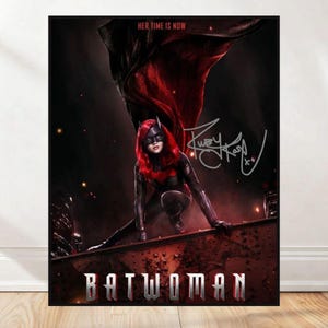 Może przedstawiać: Plakat z Batwoman w czarno-czerwonym kostiumie, klęcząca na dachu. Plakat zawiera tekst "HER TIME IS NOW" i "BATWOMAN" pogrubioną czcionką. Na plakacie widnieje podpis.