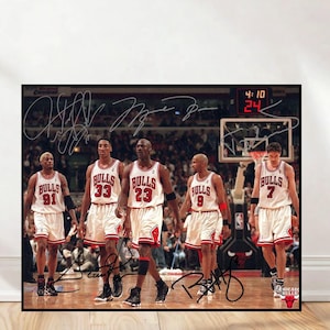 May include: A framed photograph featuring five Chicago Bulls basketball players in their white and red uniforms. The image includes player signatures and a scoreboard displaying the time 4:10 and the number 24.