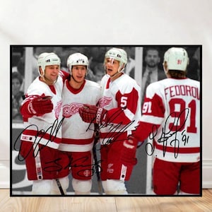 May include: A framed print featuring a group of hockey players in red and white jerseys. The players are wearing helmets and gloves, and the print includes signatures. The background is a black and white image of a hockey game.