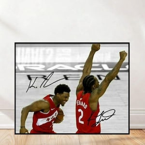 May include: A framed black and white photograph featuring two basketball players in red jerseys. One player is smiling and holding a basketball, while the other has their arms raised in celebration. Both jerseys have signatures.