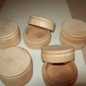 May include: Five small, round, wooden boxes with lids. The boxes are made of light wood and have a natural finish. The lids are slightly raised and have a smooth, rounded edge.
