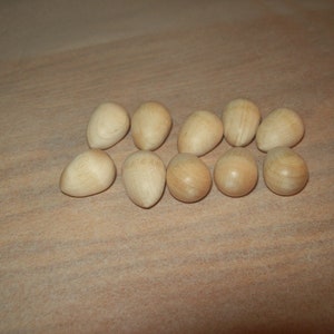 Op de afbeelding: Tien houten eieren in verschillende bruintinten, gerangschikt in een halve cirkel op een lichtbruin houten oppervlak.