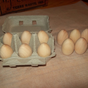 Może przedstawiać: Tekturowy pojemnik na jajka z 6 drewnianymi jajkami w środku i 6 drewnianymi jajkami na zewnątrz pojemnika. Jajka są wszystkie jasnobrązowe.