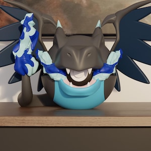 Op de afbeelding: Een donkergrijs en lichtblauw draakachtig figuurtje met grote vleugels, scherpe tanden en blauwe vlamachtige accenten. Het wezen heeft een rond lichaam, een prominente snuit en een lichtblauwe borstplaat. De tekst N3D staat linksonder.