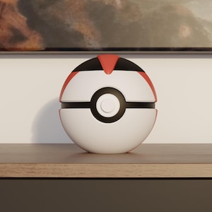 May include: A white and red Poké Ball replica with a black center band and button. The top section is red and black. The ball is sitting on a wooden surface.