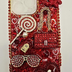 May include: Red bedazzled phone case with a variety of embellishments. Features a lollipop, purse, sunglasses, and a bottle. The case is covered in red rhinestones and glitter, with gold accents.