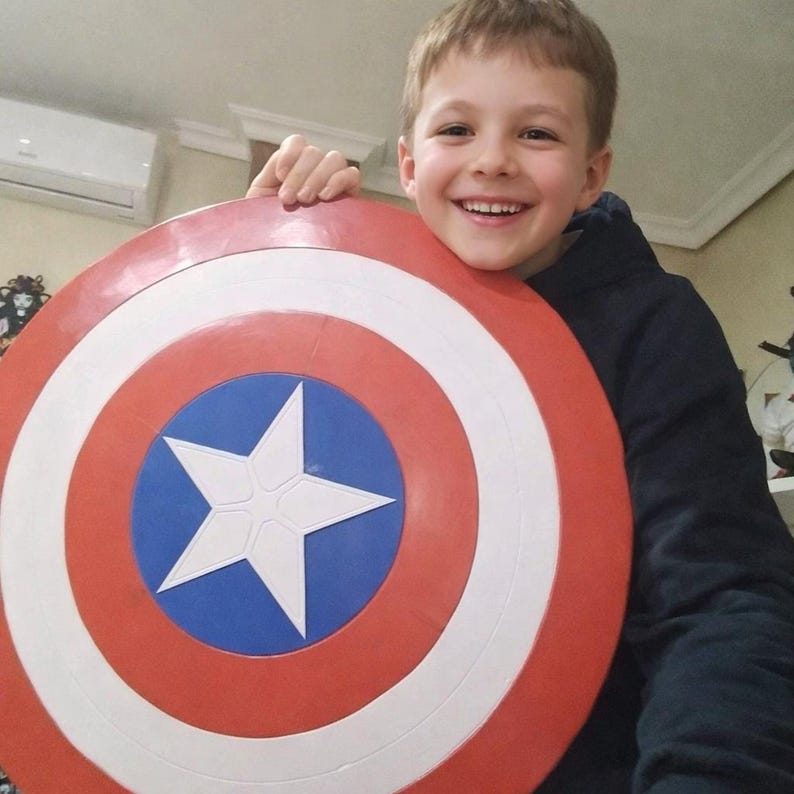 May include: A round shield with a red, white, and blue design, featuring a white star on a blue circle. The shield has concentric rings of red and white. The shield is a Captain America shield.