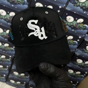 Può includere: Cappellino da baseball nero con la scritta "Sad" in bianco, impreziosito da strass. Il cappellino presenta una visiera curva e dettagli decorativi sul lato. Design classico a sei pannelli.