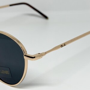 Puede incluir: Gafas de sol de metal dorado con lentes oscuras. Las monturas y varillas redondas son doradas, con un logotipo sutil en la varilla. Las lentes son oscuras y el dise&ntilde;o es cl&aacute;sico y elegante.