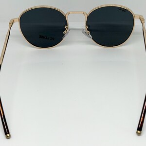 Puede incluir: Gafas de sol con montura dorada y lentes oscuras redondas. Las patillas son doradas y carey. Las gafas de sol tienen un estilo cl&aacute;sico y retro.