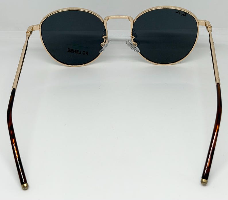 Puede incluir: Gafas de sol con montura dorada y lentes oscuras redondas. Las patillas son doradas y carey. Las gafas de sol tienen un estilo cl&aacute;sico y retro.