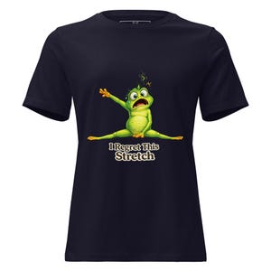 Peut inclure: T-shirt bleu marine avec une grenouille de dessin animé en grand écart et le texte "I Regret This Stretch". La grenouille est verte avec des accents jaunes, et le texte est dans une police stylisée. Le t-shirt est à col rond.
