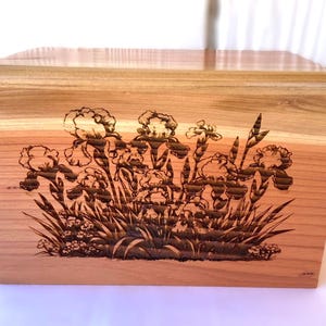 Op de afbeelding: Een houten crematie urn met een lasergegraveerd ontwerp van irisbloemen in tinten bruin en zwart.