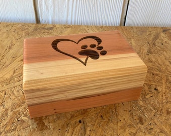 May include: A wooden box featuring a heart and paw print design. The box is crafted from cedar wood and has a natural finish.