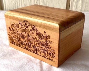 May include: A small wooden box with a floral design engraved on the front. The box is made of light brown wood and has a natural finish.
