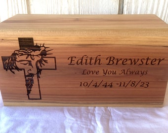 May include: A wooden cremation urn with a cross and the image of Jesus Christ engraved on the front. The urn is personalised with the name "Edith Brewster", the phrase "Love You Always", and the dates "10/4/44 - 11/8/23".