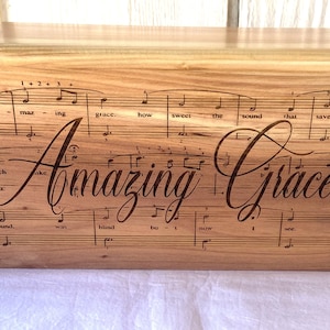 May include: A wooden box with the words "Amazing Grace" engraved on it. The box is decorated with sheet music for the hymn "Amazing Grace".