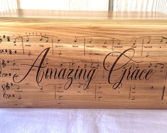 Puede incluir: Una caja de madera grabada con las palabras "Amazing Grace". La caja está decorada con partituras musicales para el himno "Amazing Grace".