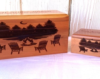 May include: Two wooden cremation urns with a campfire scene engraved on the front. The larger urn has the text "Brent Arthur Nelson" and the smaller urn has the text "Brent Arthur Nelson 1956-2021".