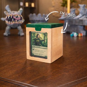 May include: A wooden card holder with a green top and a card visible in the front. The card features a woman with a bow and arrow. The word "ENGRAVED" is written on the top right of the image.