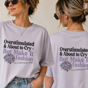 Op de afbeelding: Lila T-shirt met de tekst "Overstimulated & About to Cry - But Make It Fashion" in zwart en paars. Een hersengrafiek staat onder de tekst. Het shirt heeft ook de tekst "I have no bandwidth for your bullshit."