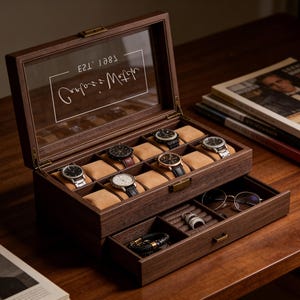 May include: A dark brown wooden watch box with a glass lid featuring the white text "Carlos's Watch" and "EST. 1987". The interior has six tan velvet watch pillows, while the pull-out drawer contains a ring holder, a black bracelet, and glasses.
