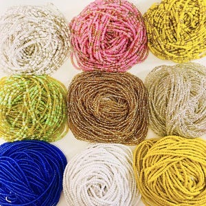 May include: Nine bundles of colorful waist beads in various colors, including white, pink, yellow, green, gold, silver, blue, and brown. The beads are small and strung together, forming coiled bundles.
